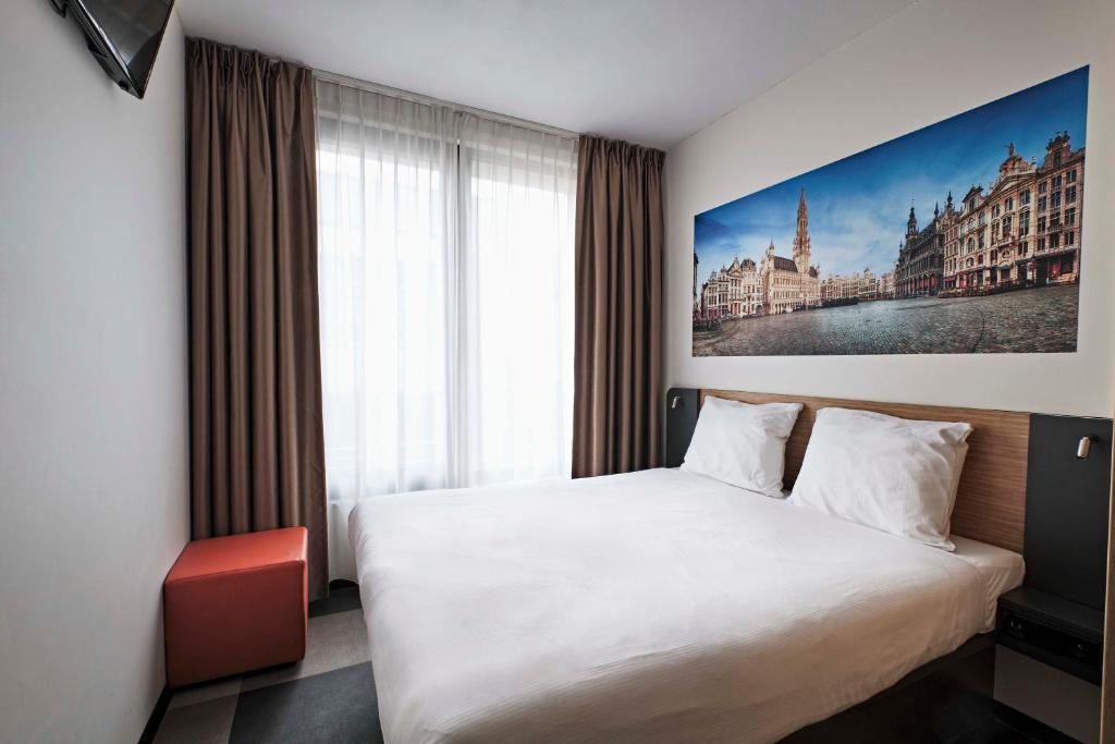 A small hotel room with a bed against a plain wall and a compact shower unit.