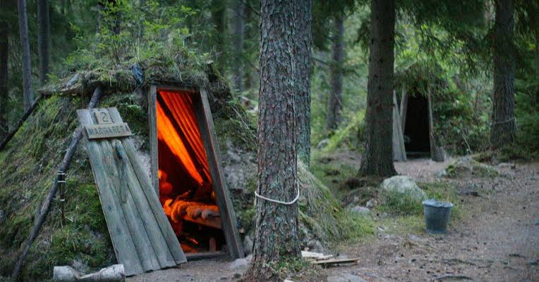 Turf-covered huts set into a wooded slope along a footpath.